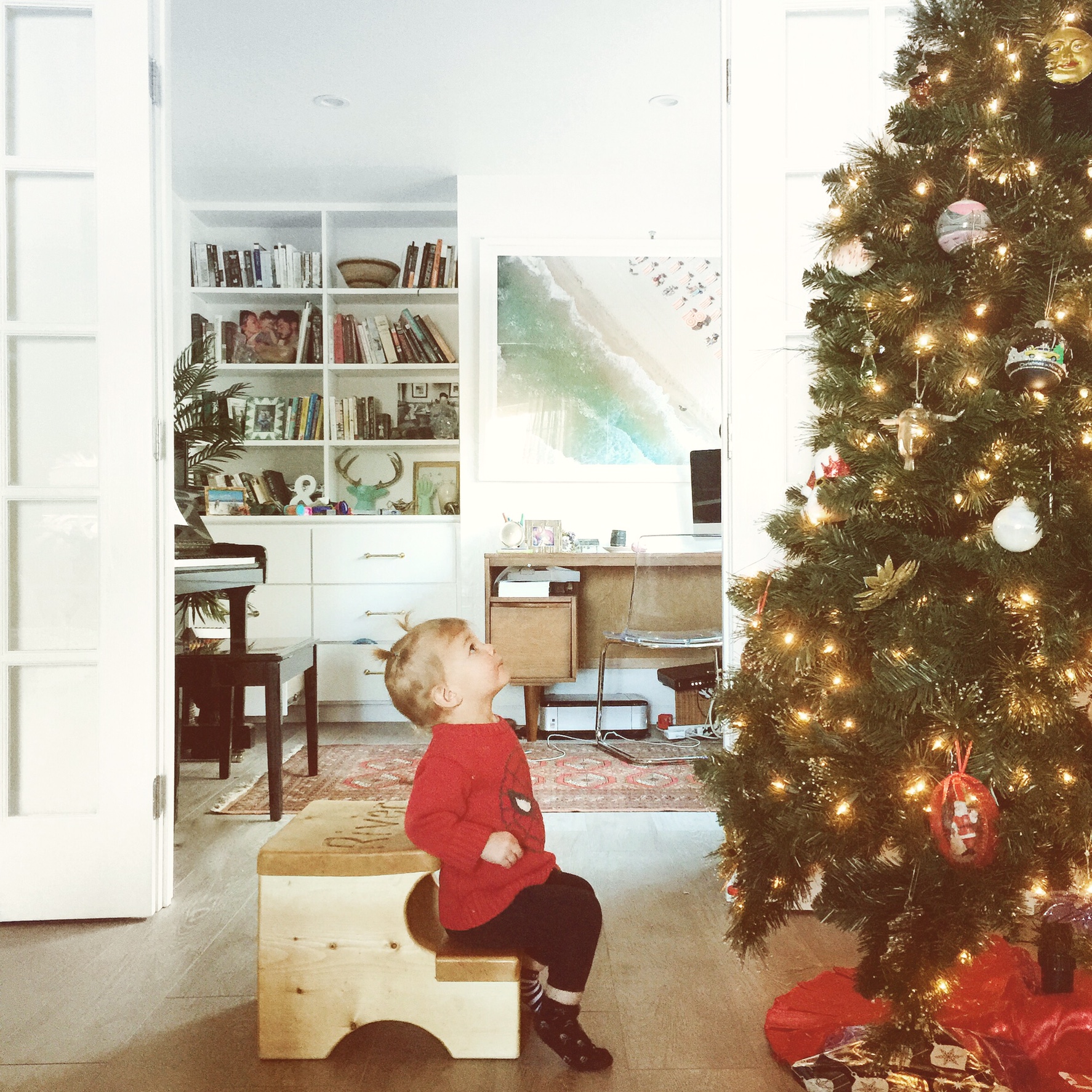 baby girl in red sweater looking at christmas tree